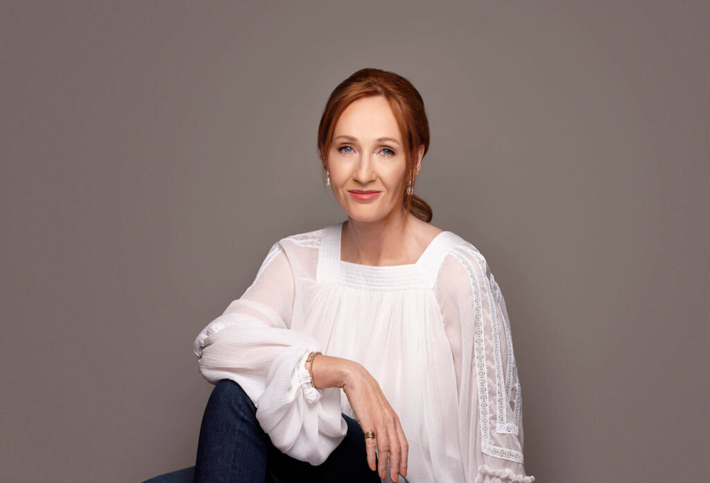 J.K. Rowling, author of the Harry Potter series, sitting and smiling in a white blouse.