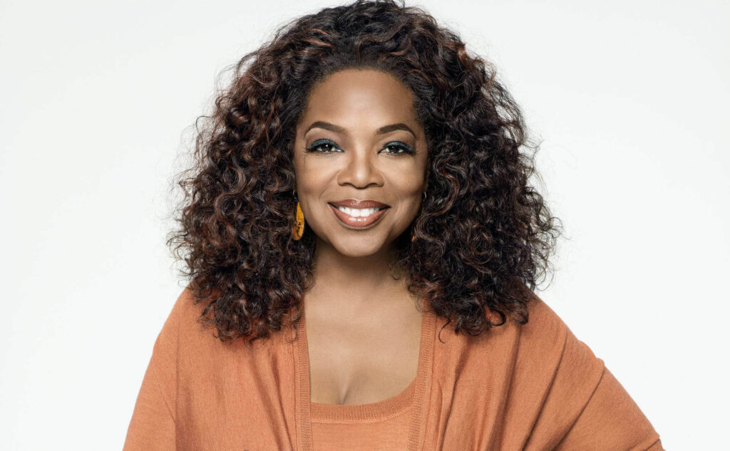 Oprah Winfrey, media mogul and philanthropist, smiling in an orange outfit.