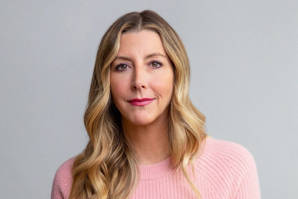 Sara Blakely, founder of Spanx, in a professional portrait wearing a pink sweater.