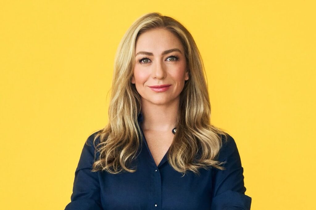 Whitney Wolfe Herd, founder of Bumble, smiling in front of a yellow background.