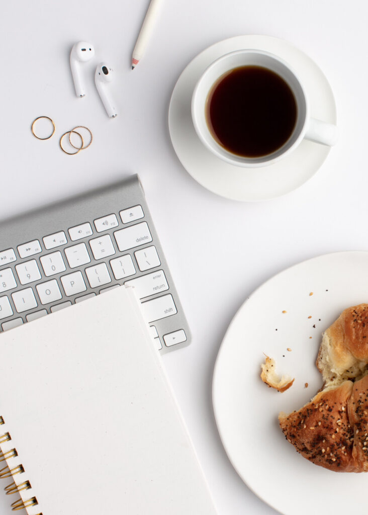 A clean flat-lay with a notebook, computer keyboard, bagel, and coffee cup—symbolizing clarity, focus, and fresh creative energy.