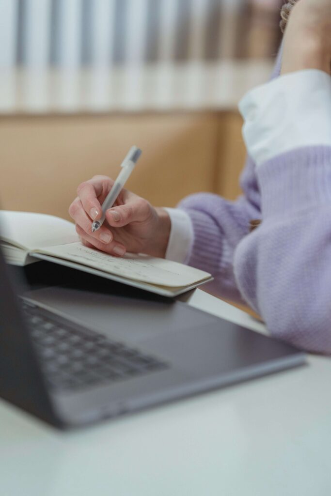 A close-up of a woman writing notes beside her laptop, capturing a calm moment of reflection—perfectly illustrating the focus and clarity of a quick website checkup.